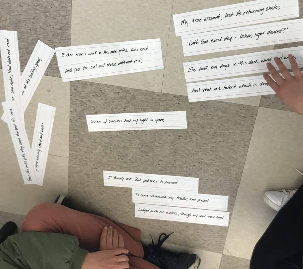 Two students sit on the floor and arrange strips of paper containing lines from a poem.